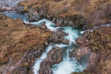 Majestic aerial drone landscape image of vibrant River Coe flowing beneath snowcapped mountains in...