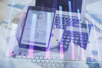 Double exposure of man's hands holding and using a digital device and forex graph drawing. Financial market concept.