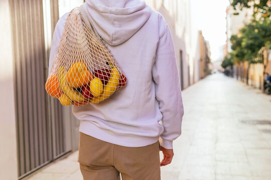 Unrecognizable man walking with groceries in mesh bag