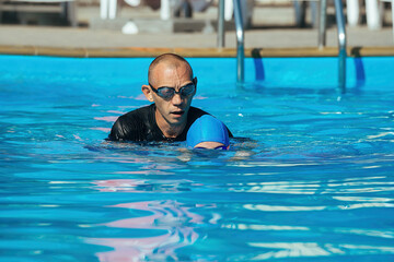 A swimming coach conducts an individual lesson for a little girl, teaches her how to swim correctly in the water of the pool in the warm season