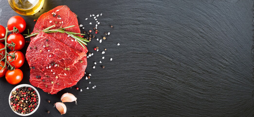 Raw beef steak with spices and ingredients for cooking on black slate background. Banner for...