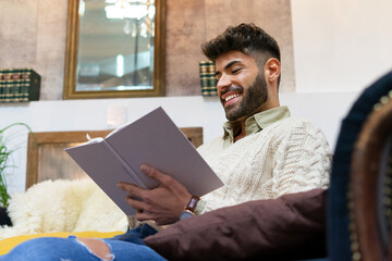 Positive young Hispanic guy reading interesting book at home