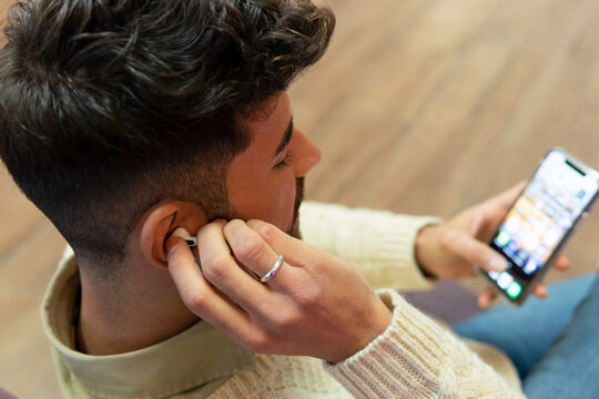 Young ethnic man with wireless headphones on smartphone at home