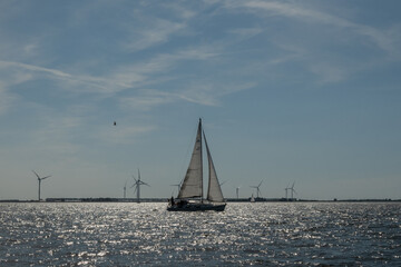 The power of wind. a sail boat in the foreground propelled on the water by wild in the same way as the turbines in the background generate clear sustainable power for public usage