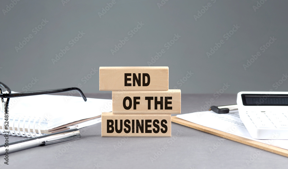 Aufkleber end of the business text on a wooden block with notebook,chart and calculator, grey background