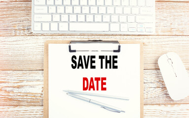 SAVE THE DATE text on a clipboard with keyboard on wooden background