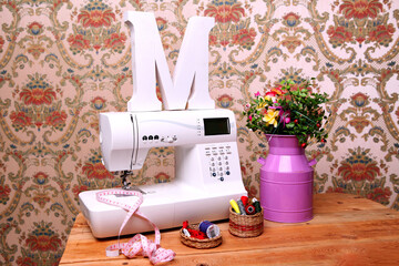 Composition from a sewing machine. Mannequin, flowers on a retro table and threads. Sewing supplies and composition with a sewing machine in the interior. With the letter M. for the fashion magazines