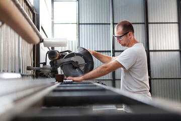 Man on a workplace cutting aluminium bar with a circular saw, workshop interior