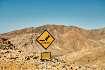 Road sign with squirrel illustration against sandy mountains