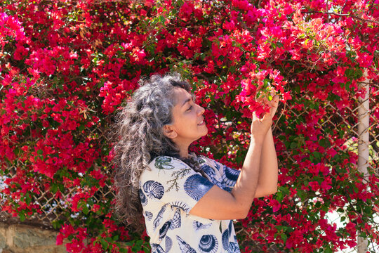 Smiling ethnic woman touching blooming Bougainvillea in town