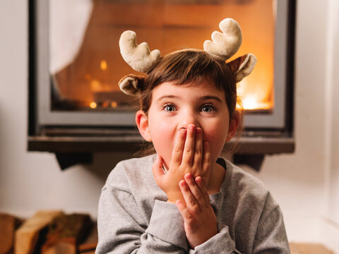 Amazed girl in reindeer antlers covering mouth