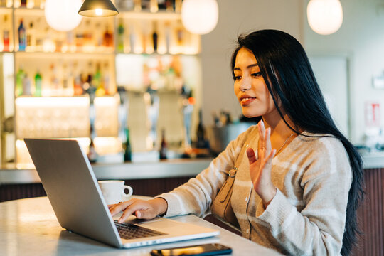 Asian woman having video chat on laptop in cafe