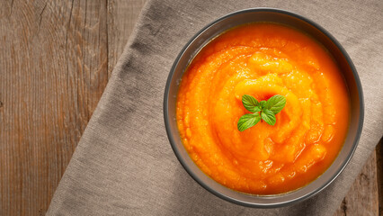 Delicious pumpkin and carrot soup in bowl on old wooden table