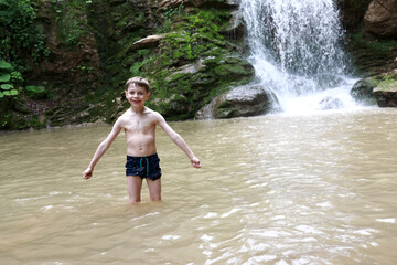 Child posing in Rufabgo stream next to waterfall Shum