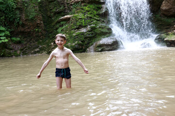 Fototapeta premium Child posing in Rufabgo stream next to waterfall Shum