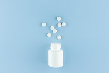white round pills scattered from a white plastic jar on a blue background