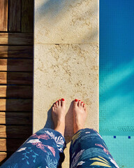 Pies descalzos de mujer con las uñas rojas en el borde de una piscina