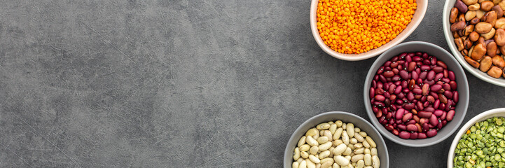 Banner of different types of legumes in bowls, yellow and green peas and lentils, colored beans and maash, top view, copy space