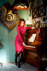 A girl in a red dress stands at a musical instrument piano.