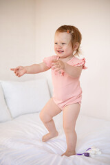 Fototapeta premium Cute cheerful red-haired baby plays on the bed. Outdoor games at home. Light background. Lifestyle