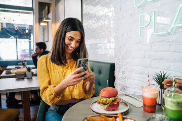 Crop blogger taking photo of hamburger on smartphone in restaurant