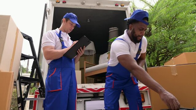 Two delivery men carrying and checking cardboard box in new home