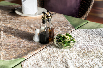 A condiment set is set on the wooden table with the shadow of the bottle lay down on the table cloth.