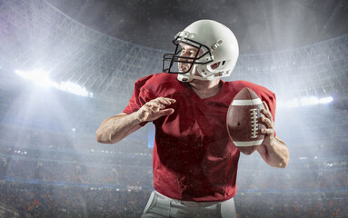 Football sportsman player with ball in action on stadium under lights of background. Sport, proud footballer in white helmet and red t-shirt ready to play.