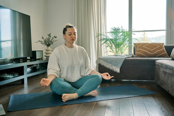 Woman doing online yoga at home. Female trener teaches asana in video conference. Health care, authenticity, sense of balance and calmness. - obrazy, fototapety, plakaty