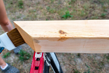 Naklejka premium The woman impregnates raw planed wooden pine beams with dimensions of 100x100mm with a colorless impregnation.