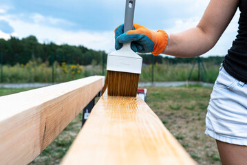 The woman impregnates raw planed wooden pine beams with dimensions of 100x100mm with a colorless impregnation.
