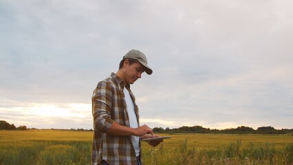 Farmer with a tablet computer in front of a sunset agricultural landscape. Man in a countryside field. Country life, food production, farming and technology.