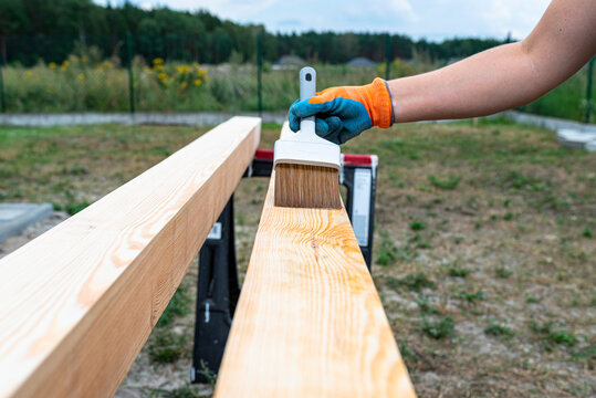 The woman impregnates raw planed wooden pine beams with dimensions of 100x100mm with a colorless impregnation.