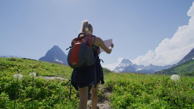 Iconic scenery of Glacier National Park, Montana, USA. Woman with a backpack hiking along mountainous trail with a map in her hands. High quality 4k footage