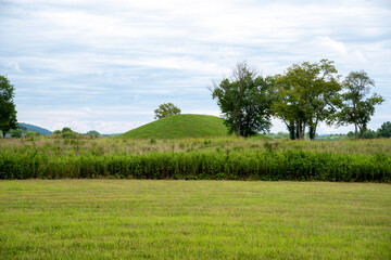 Prehistoric Native North American earthen burial mound seen from grass area in meadow. Large Native American prehistoric earthwork burial mound at Seip Earthworks, Ohio. Dramatic sky and mowed grass. - obrazy, fototapety, plakaty