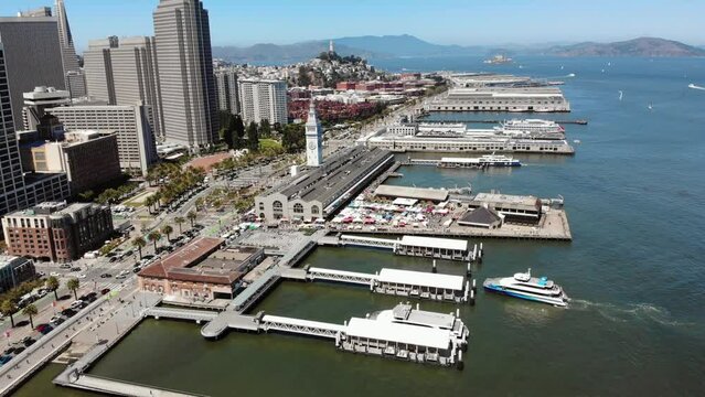 Aerial flight over port of San Francisco during ferry docking during sunny day - Ferry Building and skyscraper in background