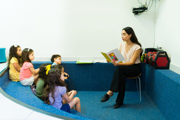 Dedicated teacher reading a fairy tale book to her kids students