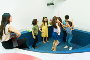 Excited preschool children dancing along an education son at school