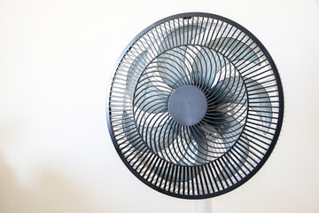 A spinning black electric fan isolated on right against white wall, cooling down interior during...