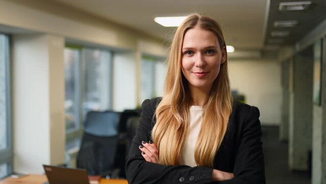 Smiling caucasian business woman in formal outfit looking at camera standing in office. Portrait of happy pretty businesswoman in jacket. Condfident female corporate worker with arms crossed on chest.