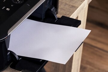 A close up portrait of a printer with an empty white piece of paper in its printed output tray. The blank page can be used to display some print out.