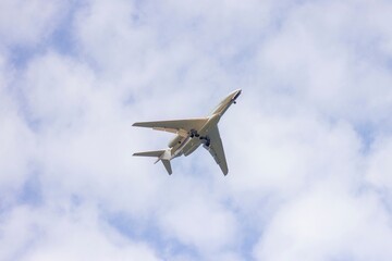 A portrait from below of a private plane flying in a cloudy sky. The jet plane has started to descend for landing and the wheels are out.