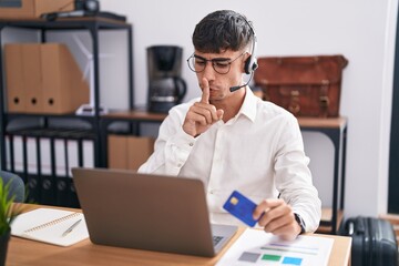 Young hispanic man working using computer laptop holding credit card asking to be quiet with finger on lips. silence and secret concept.