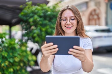 Fototapeta premium Young blonde woman smiling confident watching video on touchpad at street