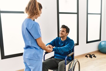 Obraz premium Young disabled man and physiotherapist smiling happy shaking hands at the clinic.