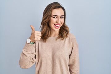 Young woman standing over isolated background doing happy thumbs up gesture with hand. approving expression looking at the camera showing success.