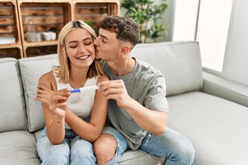 Young caucasian couple smiling happy holding pregnacy test at home.