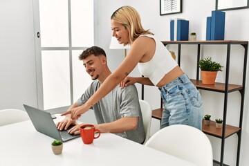 Fototapeta premium Young caucasian couple using laptop and drinking coffee sitting on the table at home.