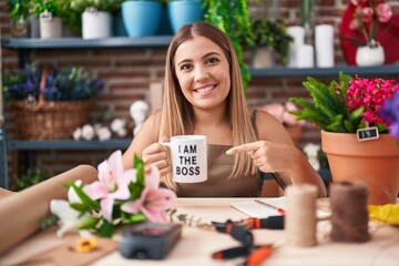 Young blonde woman working at florist shop holding i am the boss cup smiling happy pointing with hand and finger