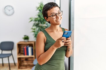 Young hispanic woman smiling confident using smartphone standing at waiting room